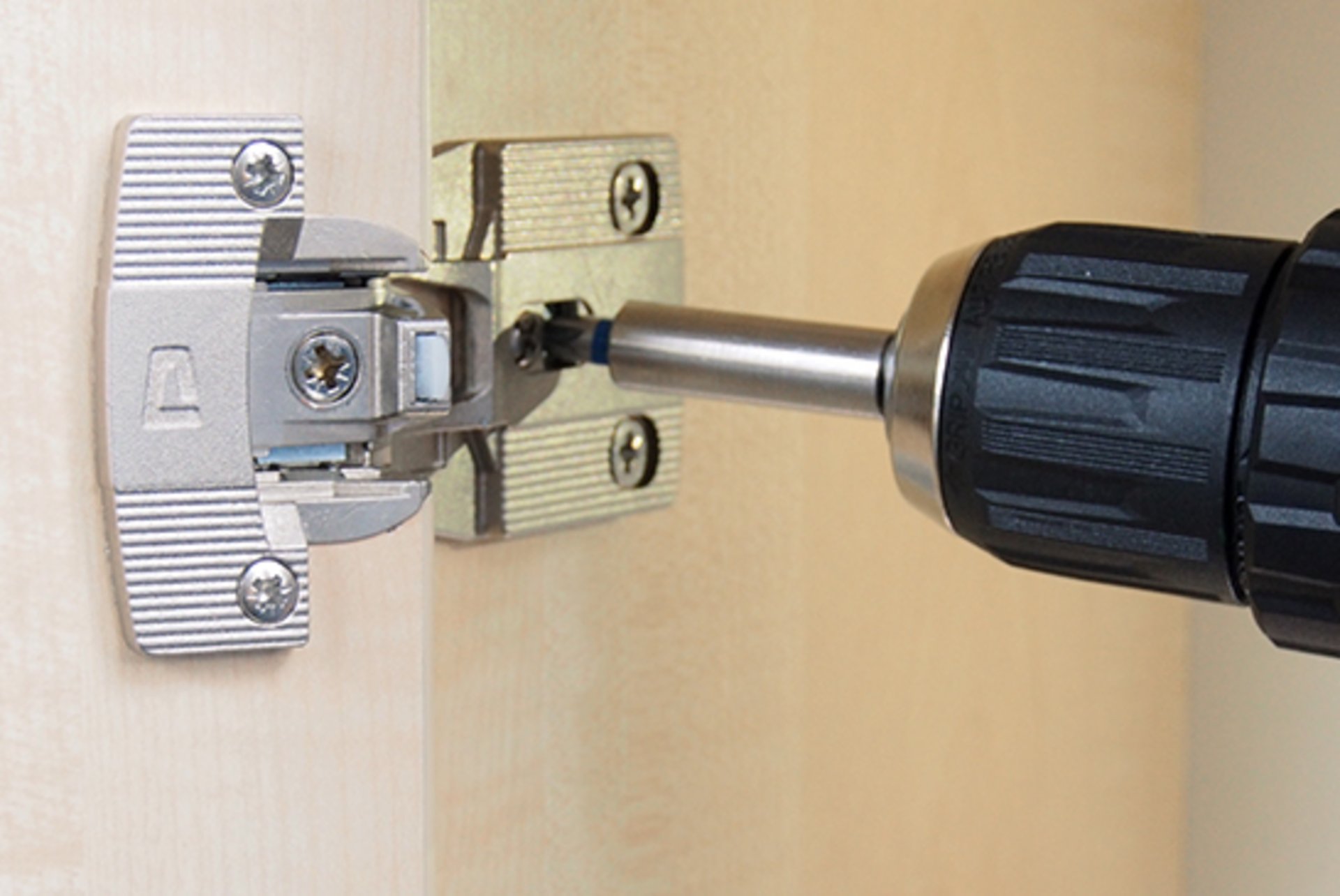 Ein Scharnier von PRÄMETA Präzisionsmetall wird mit einem Akkuschrauber an einem Holzschrank befestigt.