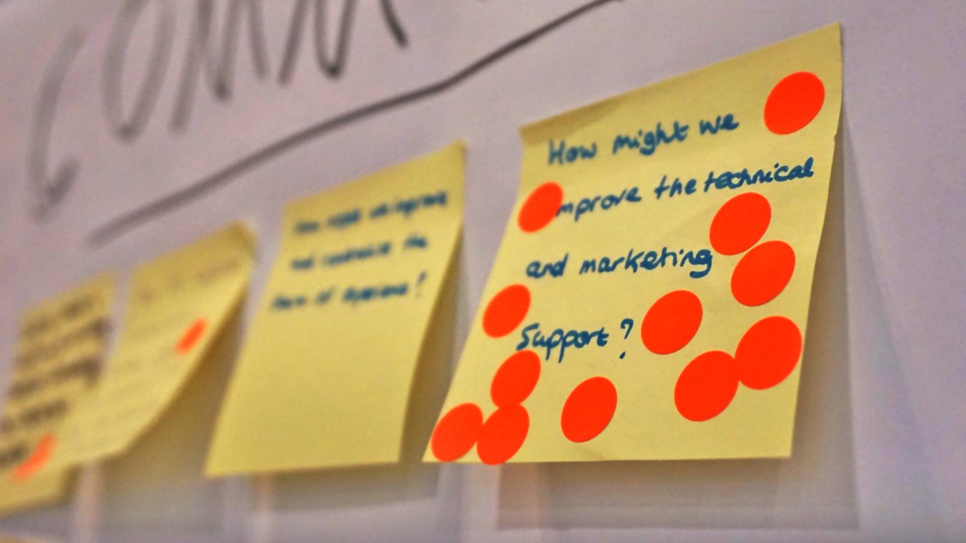 Post-Its mit Ideen und Klebepunkten aus einem Design Thinking Workshop heften an einer Wand.