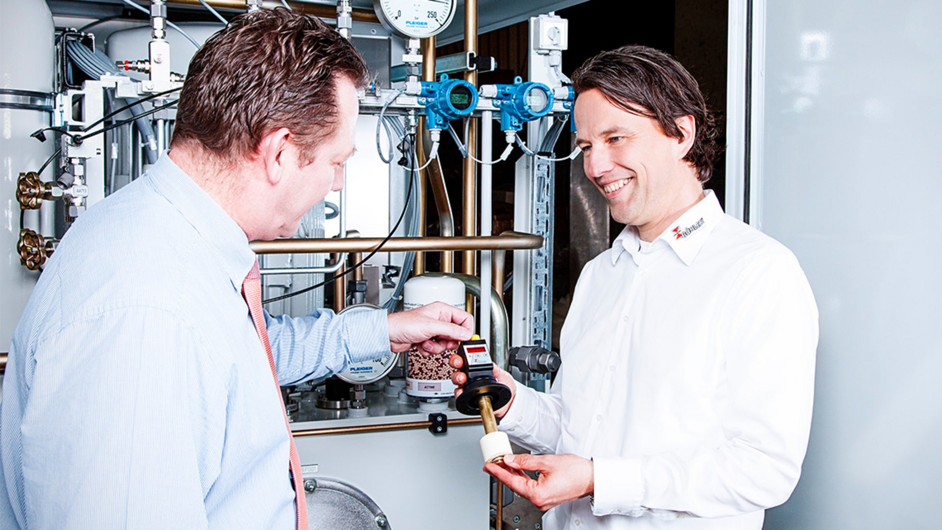 Die BÜHLER Technologies Bildwelt zeigt eine Kunden Beratung mit Produkt vor einer Anlage.