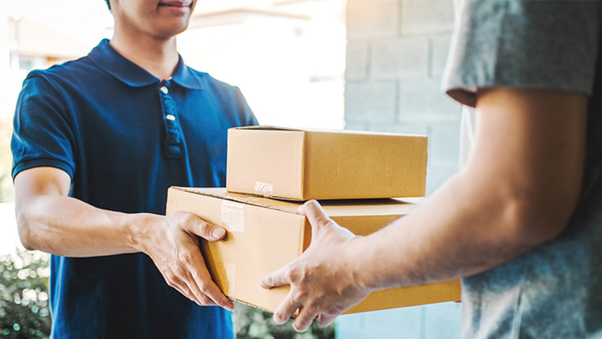 Der Bote eines Lieferdienstes übergibt an der Haustür zwei Pakete an den Empfänger.