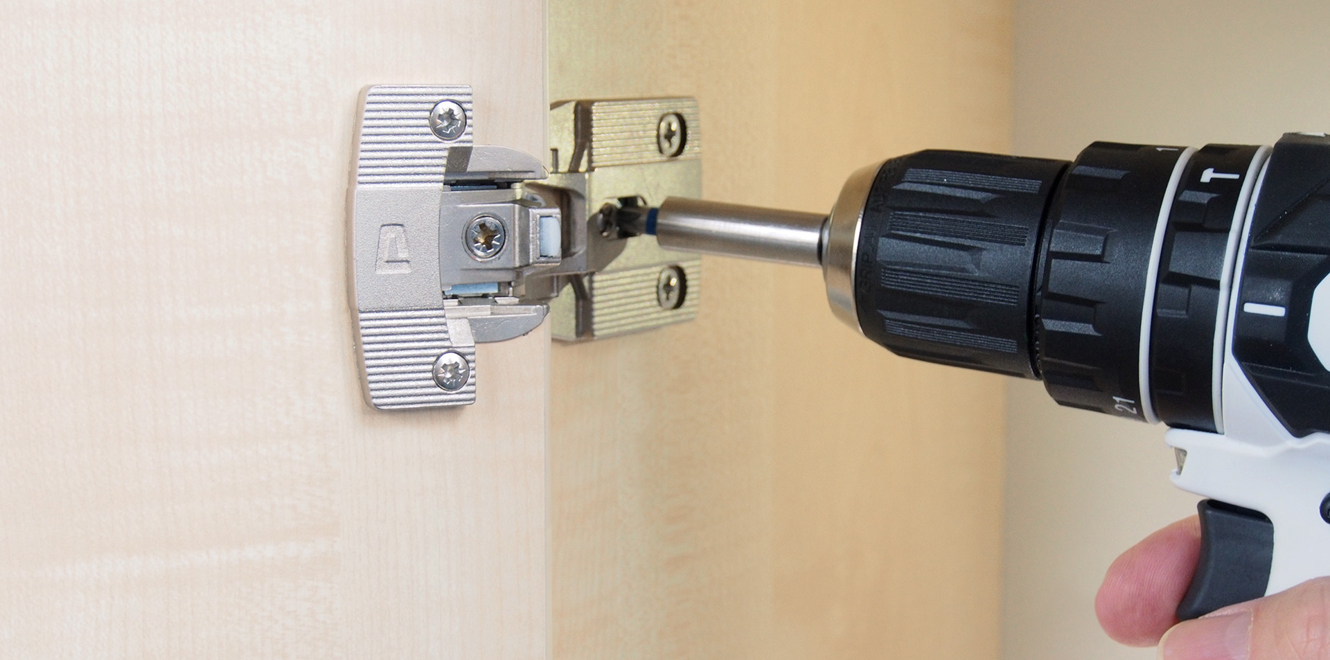 Ein Scharnier von PRÄMETA Präzisionsmetall wird mit einem Akkuschrauber an einem Holzschrank befestigt.